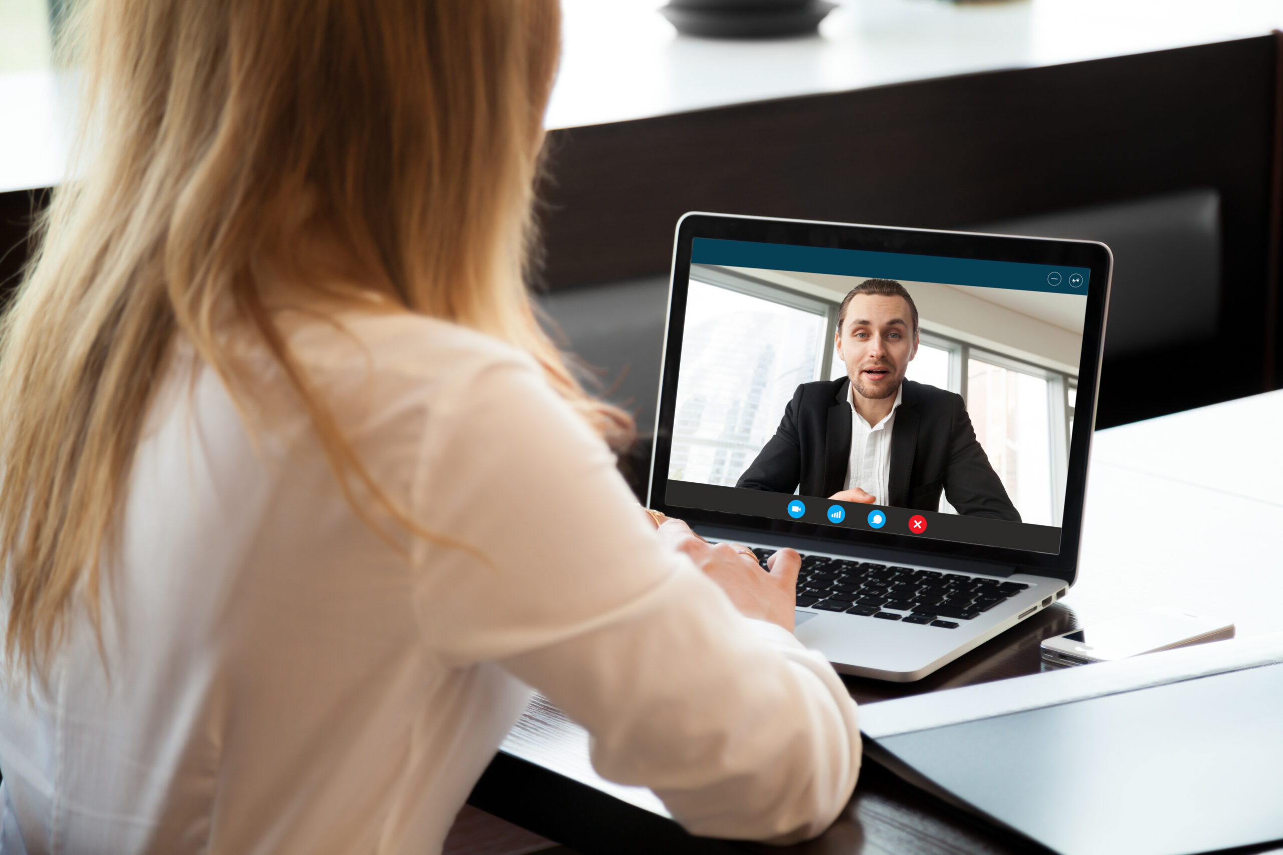 A female person, video conferencing a make person. The image shows the back of her head and back, and shows his image on her laptop.